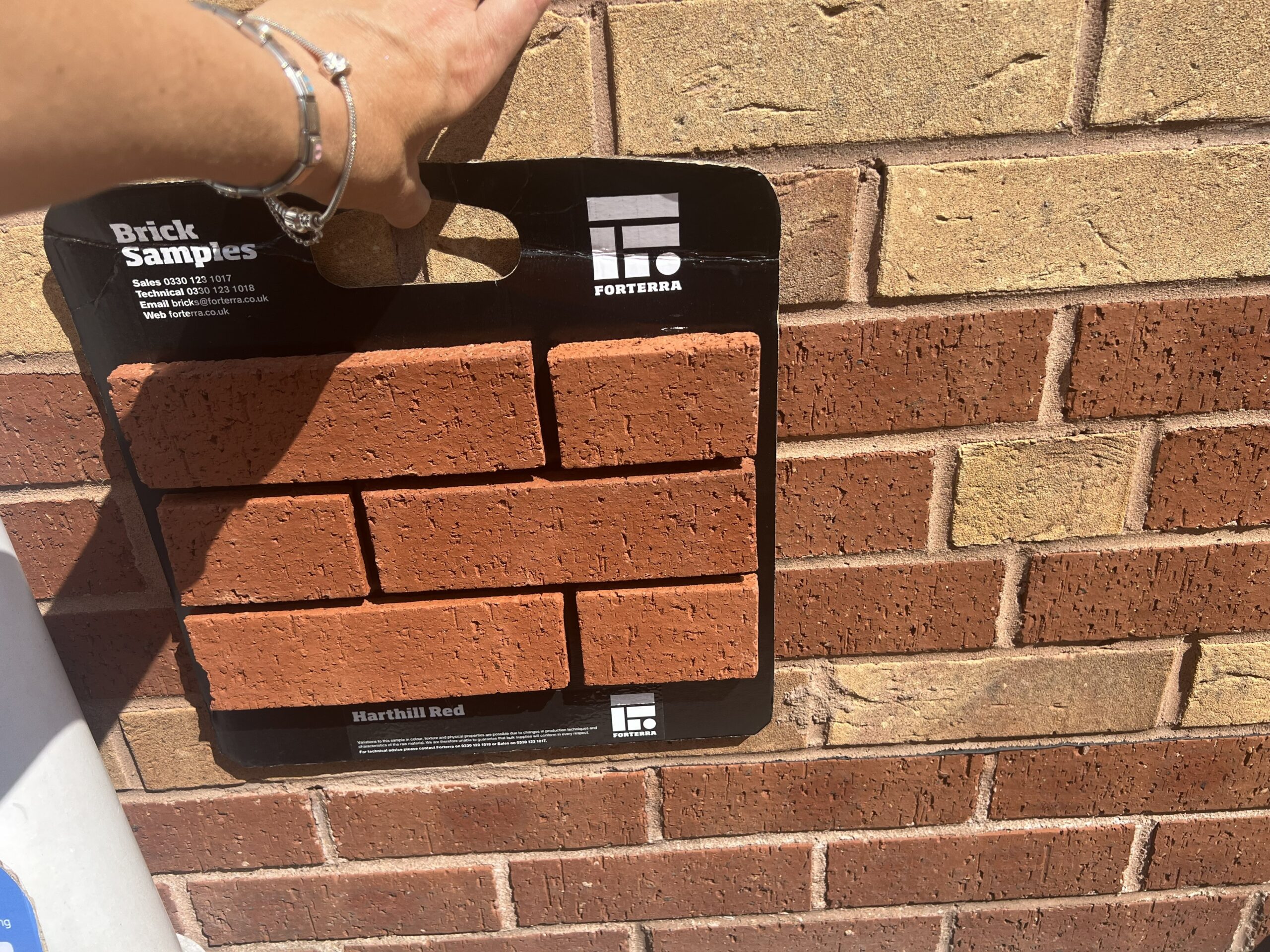 Image is a sample panel of red bricks held against a wall