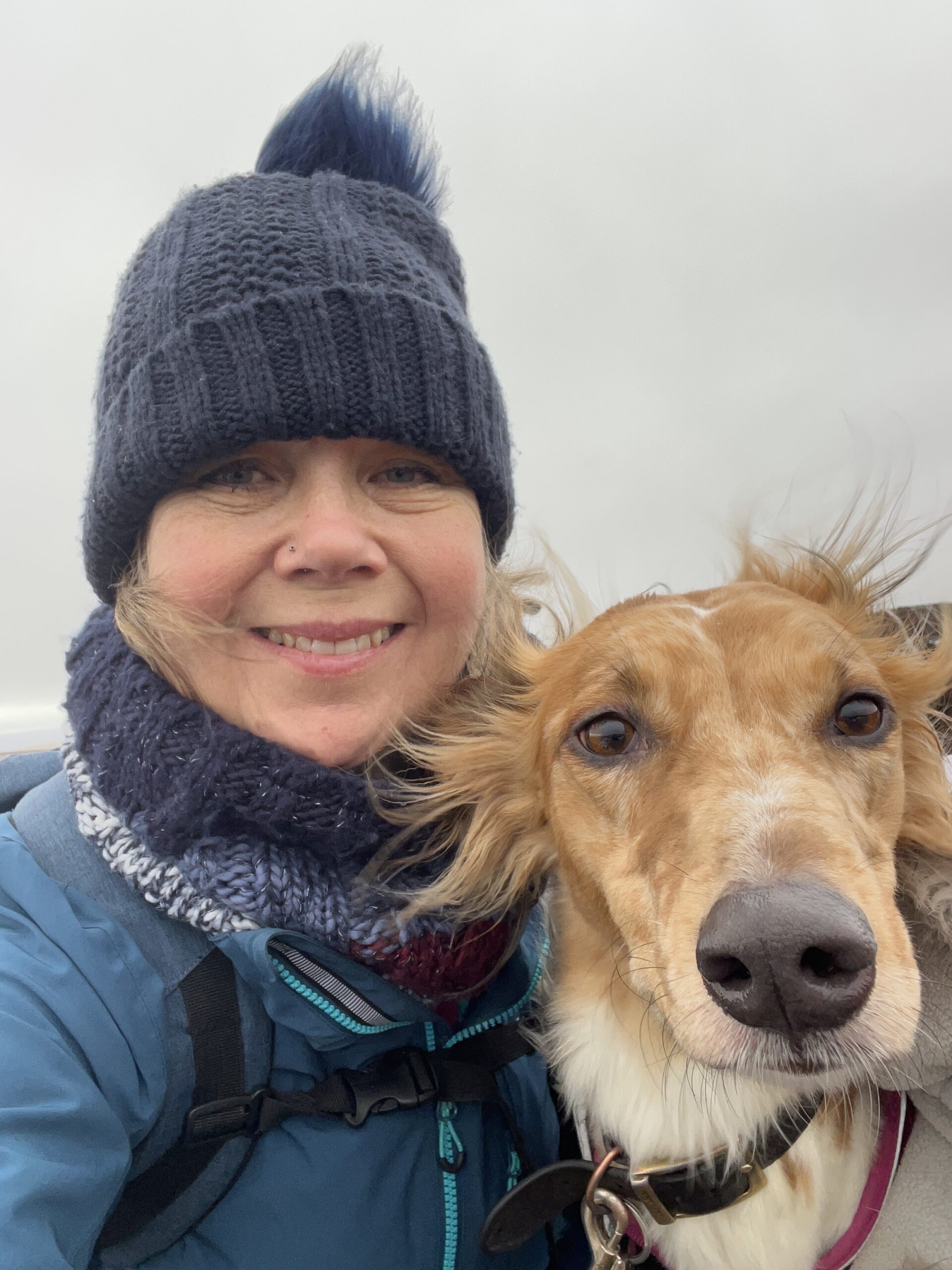 Selfie of me and Nellie, my dog, on a winter's walk. I have a blue woolly hat and coat on and the sky is grey and overcast