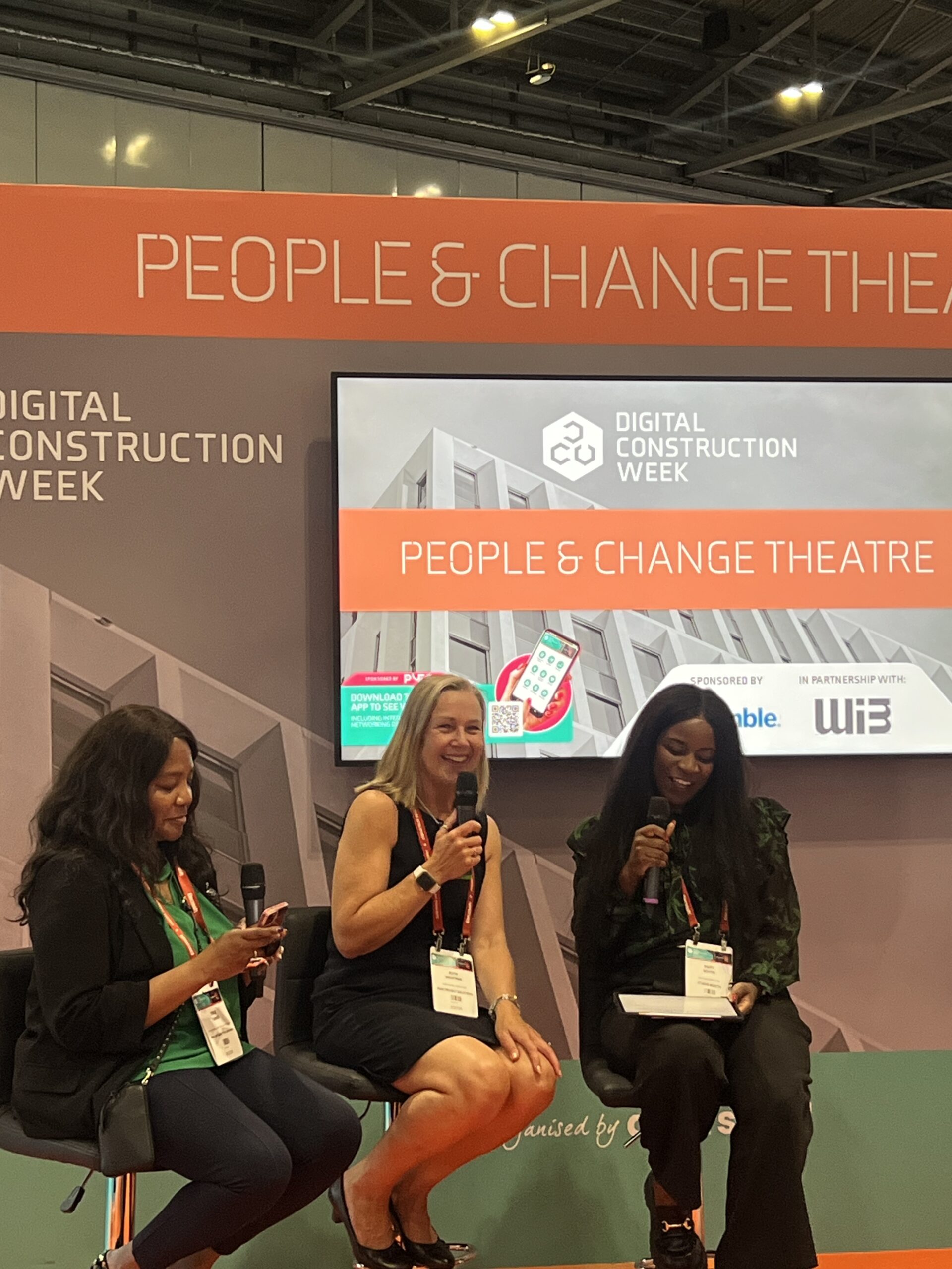 Ruth sitting on a tall stool taking with a panel of 2 other women at a construction conference