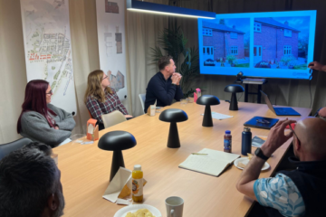Image is of a room with people sitting around a large table looking at a presentation delivered by Ruth Wightman